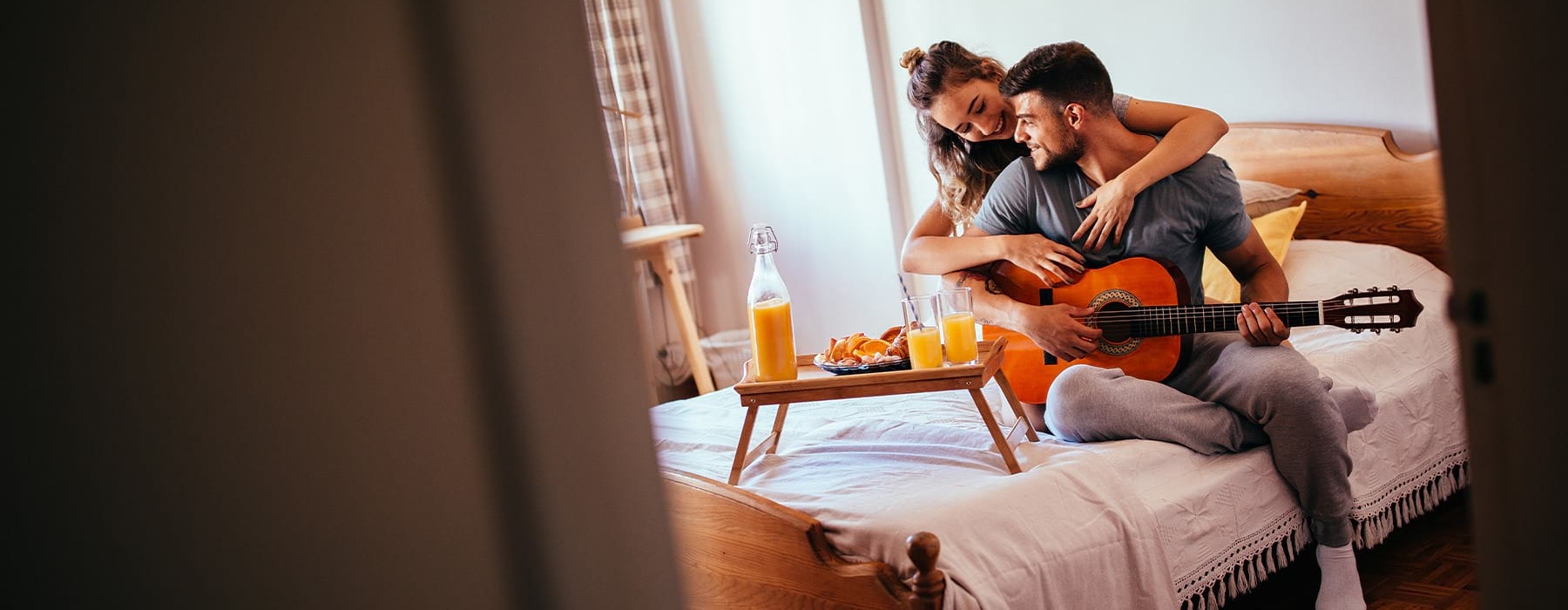 A couple is sitting on the bed playing an acoustic guitar.